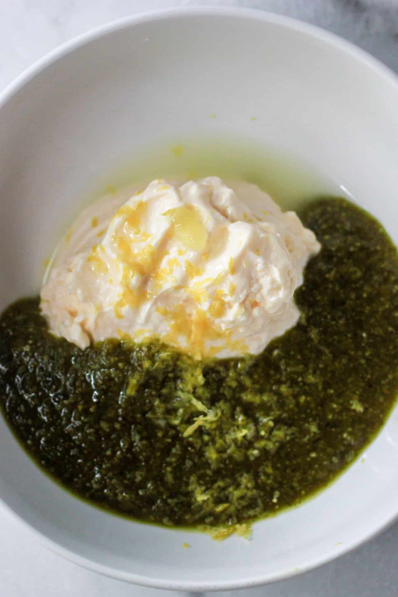 Pesto, mayonnaise, lemon and lemon zest to make pesto potato salad in white bowl.