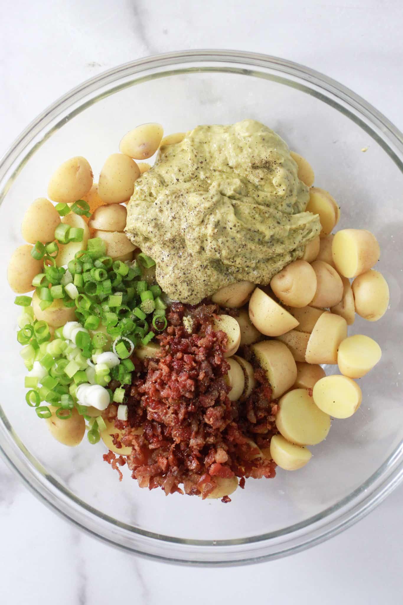 The ingredients to make Pesto Potato Salad in large glass bowl before incorporating ingredients.