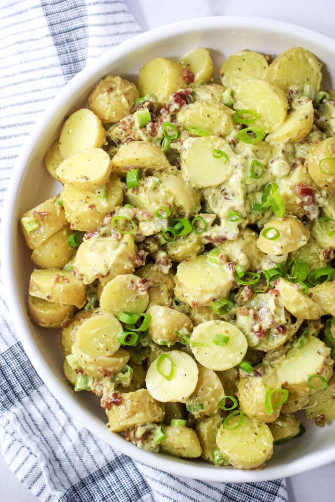Pesto potato salad with bacon and green onions in a white serving bowl.