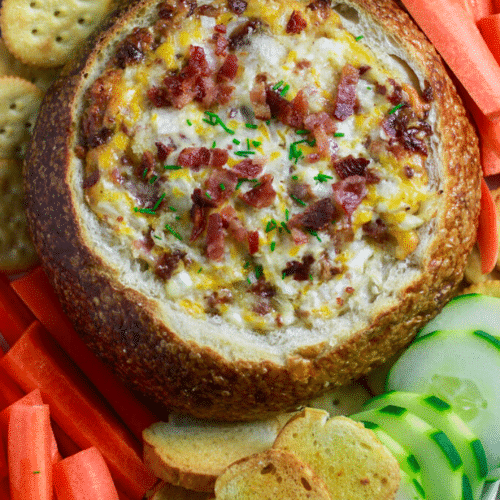 Cheesy Bacon Dip Recipe in a bread bowl with vegetables and crackers.