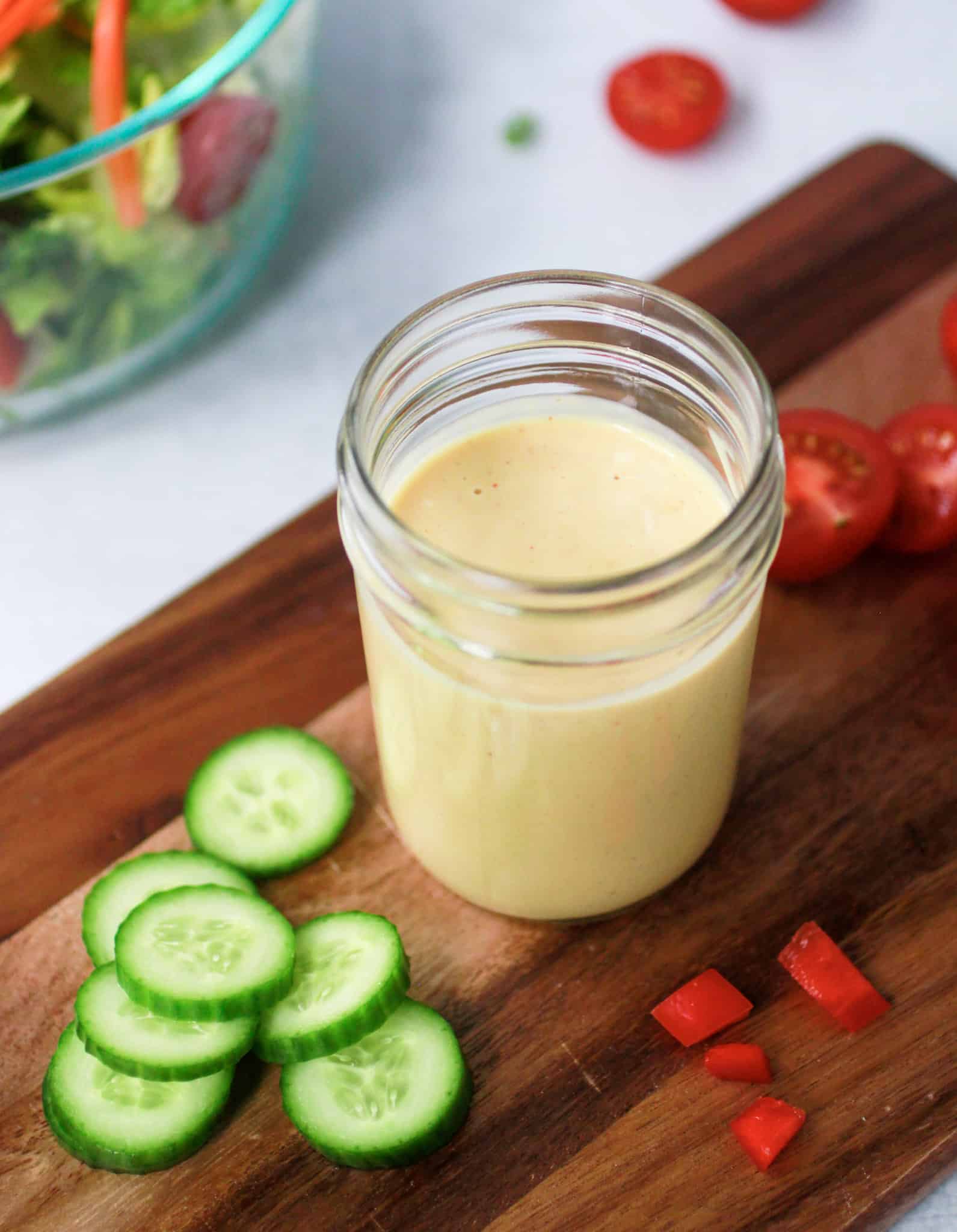 Honey mustard dressing in a jar with vegetables on a cutting board.
