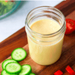 Honey Mustard Dressing in a mason jar with cucumbers and tomatoes.