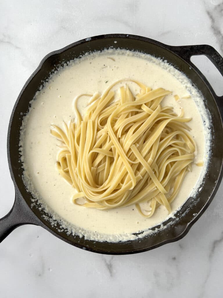 Alfredo sauce with fettuccine noodles in a cast iron skillet.