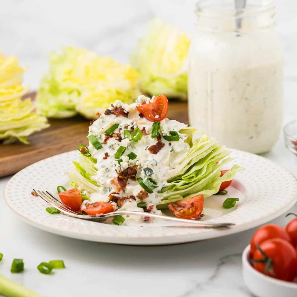 A classic wedge salad on a plate with tomatoes, bacon and green onions.