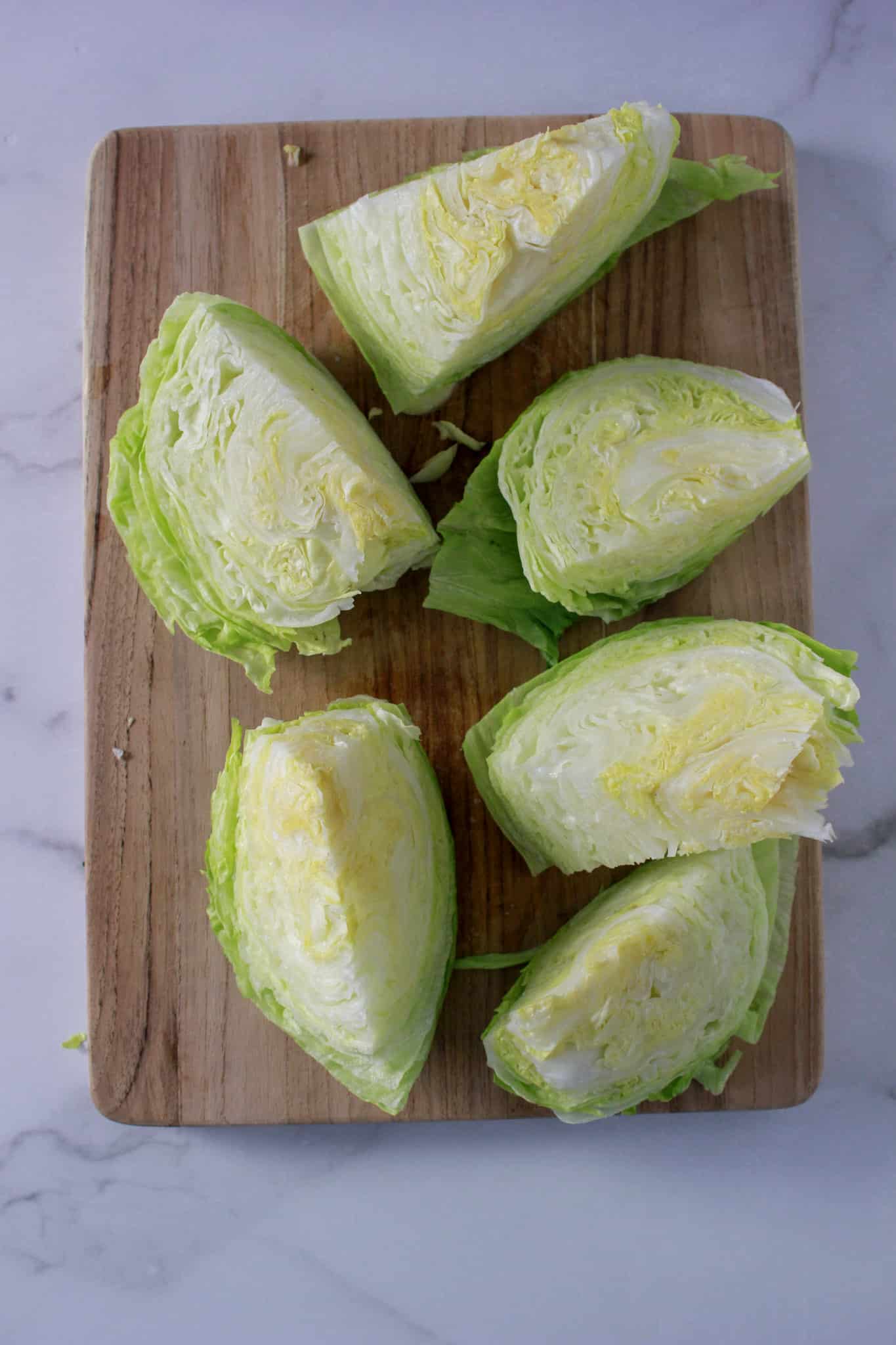 A head of iceberg lettuce on a wooden board cut in to six wedges for a classic wedge salad.