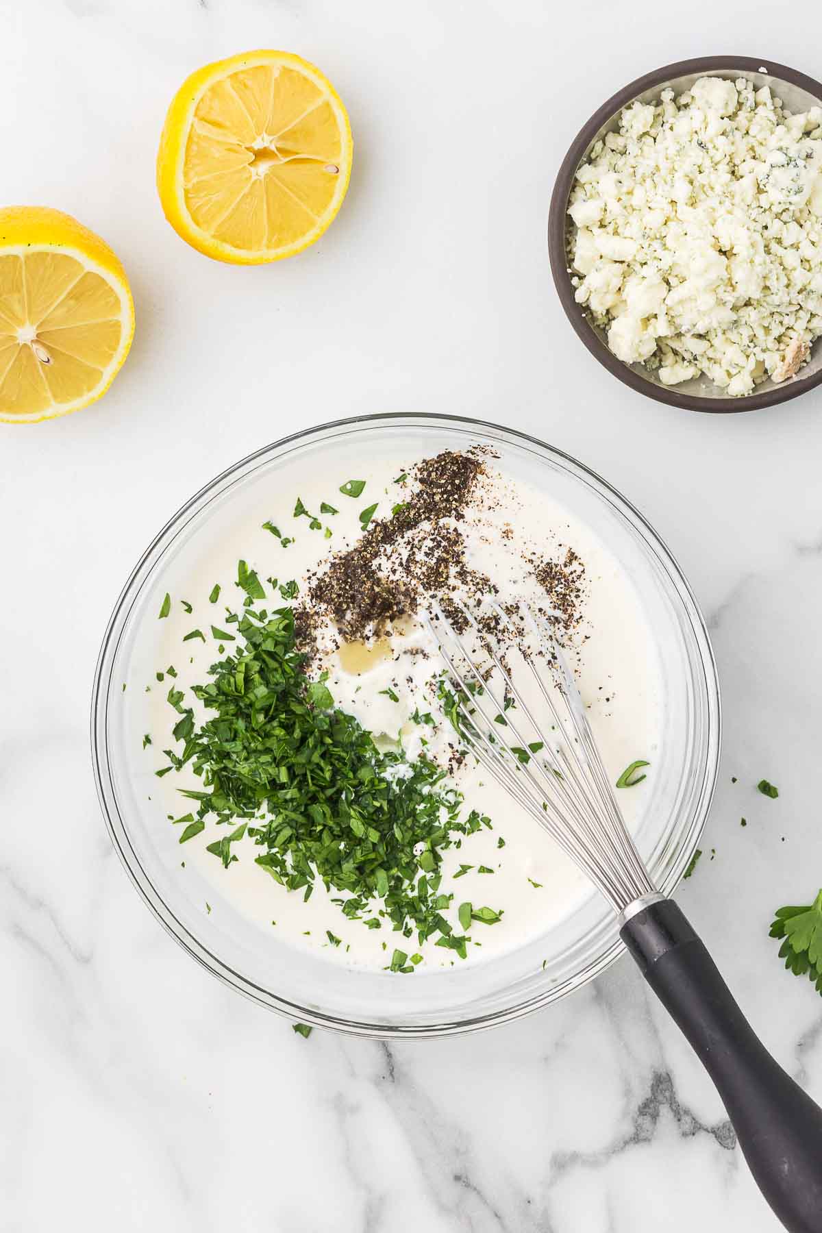 Mixing bowl with mayonnaise, buttermilk, lemon juice, parsley, and black pepper for homemade blue cheese dressing.
