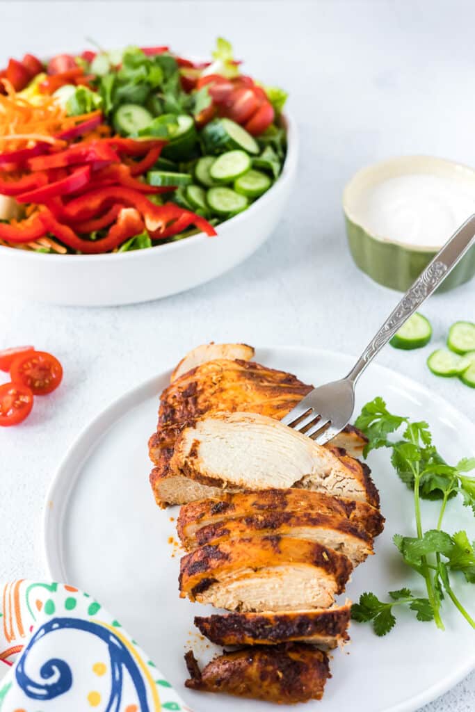 Mexican chicken breast on a plate with a salad in the background.