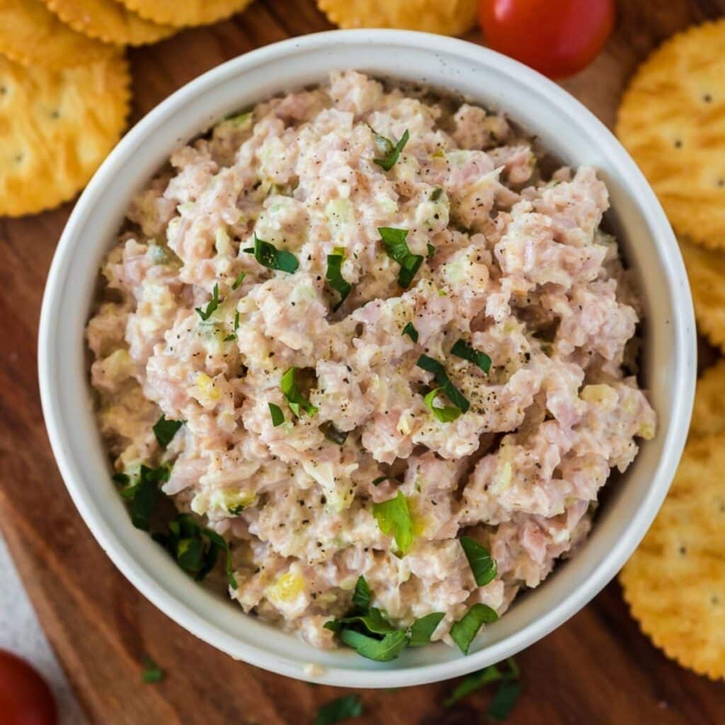 Old Fashioned Ham Salad in a bowl with crackers around it on a cutting board.