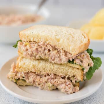 Ham salad on white bread with lettuce on a white plate.