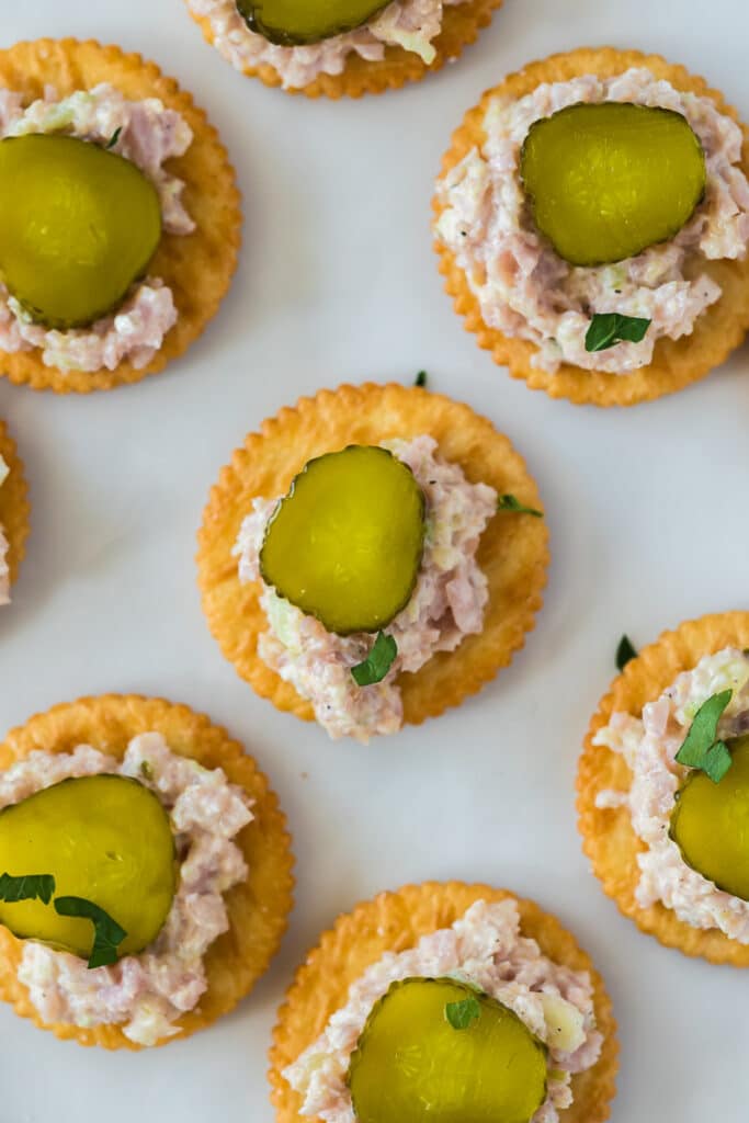 Ham salad on top of ritz crackers with a dill pickle on top.