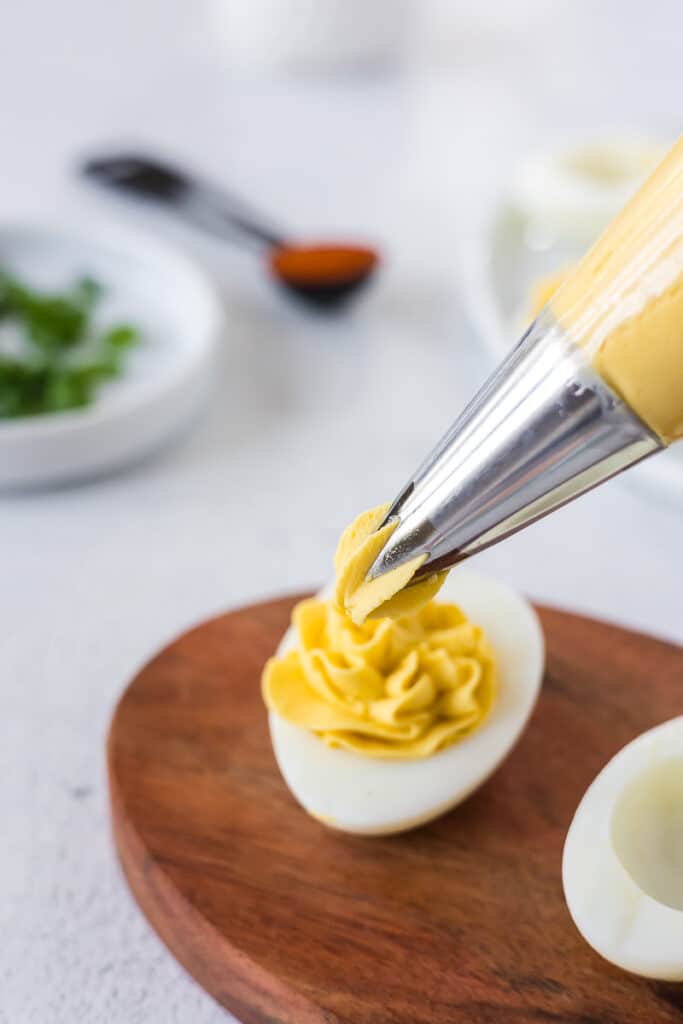 The filling for deviled eggs being piped into the white part of an egg.