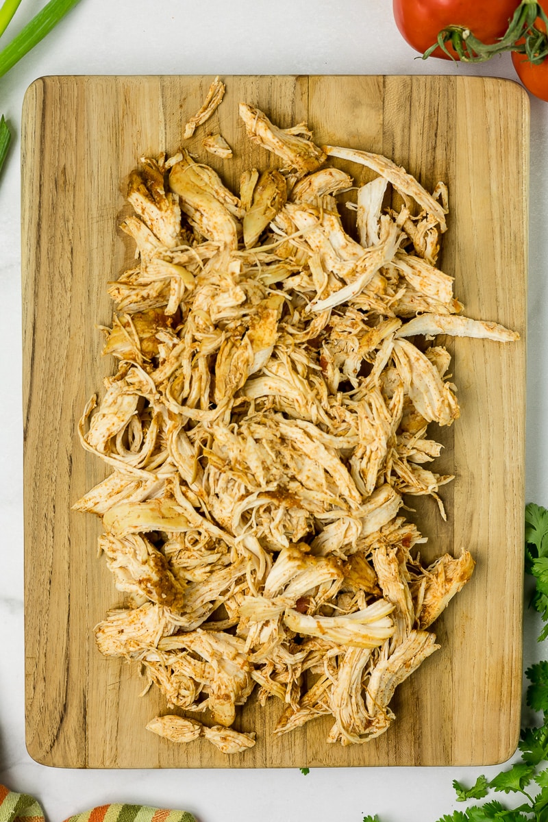Cooked salsa chicken shredded on a wooden cutting board.