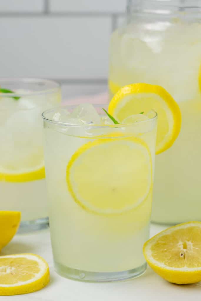 Two glasses of fresh squeezed lemonade with lemons as garnish.