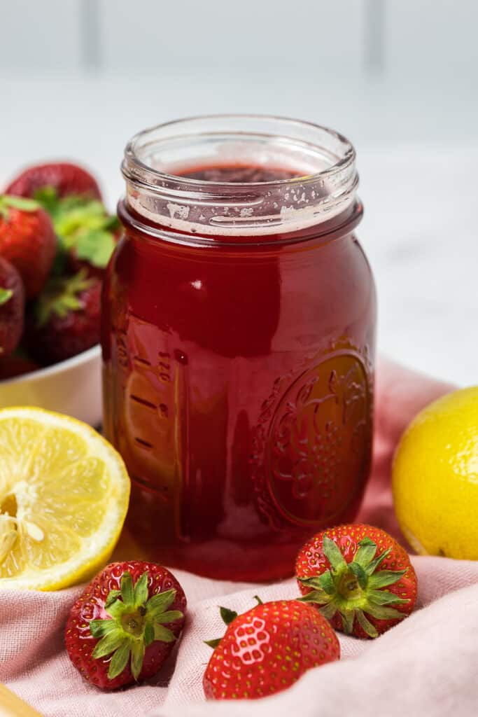 Strawberry Simple Syrup in a canning jar with fresh fruit around it.