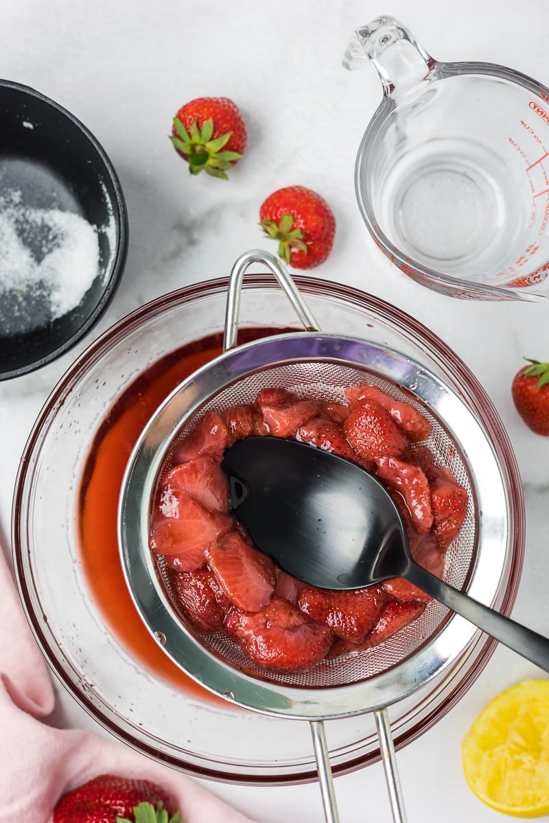 Strawberries in a strainer with a spoon to get all of the juice from the strawberries.