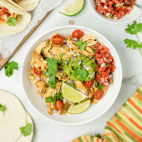 Salsa Chicken in a bowl with avocado, pico and lime wedges.