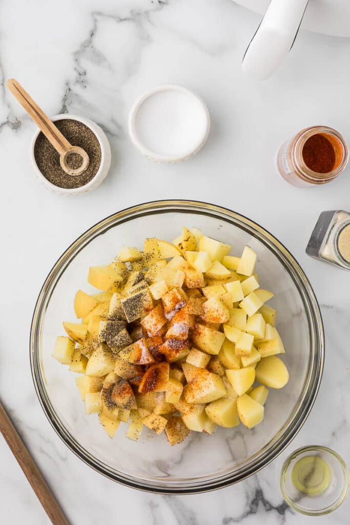 Diced potatoes in a bowl with olive oil and spices.