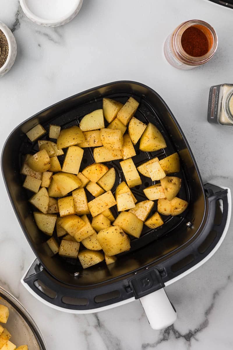 Seasoned potatoes in an air fryer basket before cooking them.