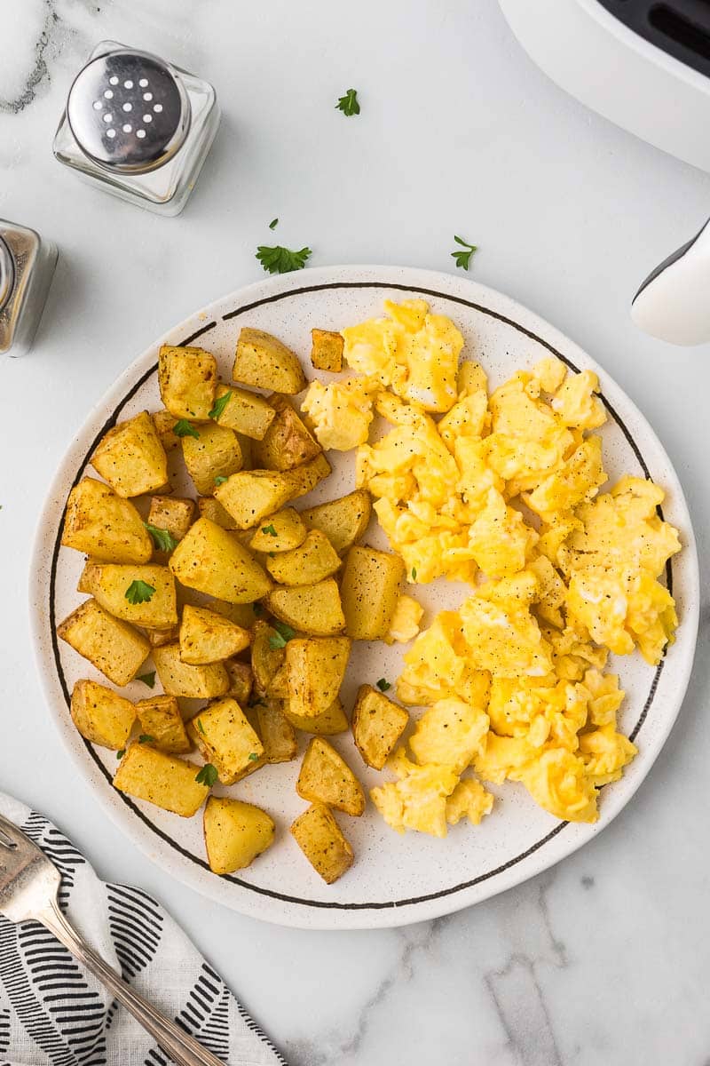 Perfect breakfast burritos made in the air fryer on a plate with scrambled eggs.