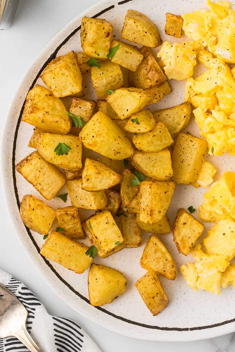 Breakfast potato recipe on a plate with scrambled eggs.