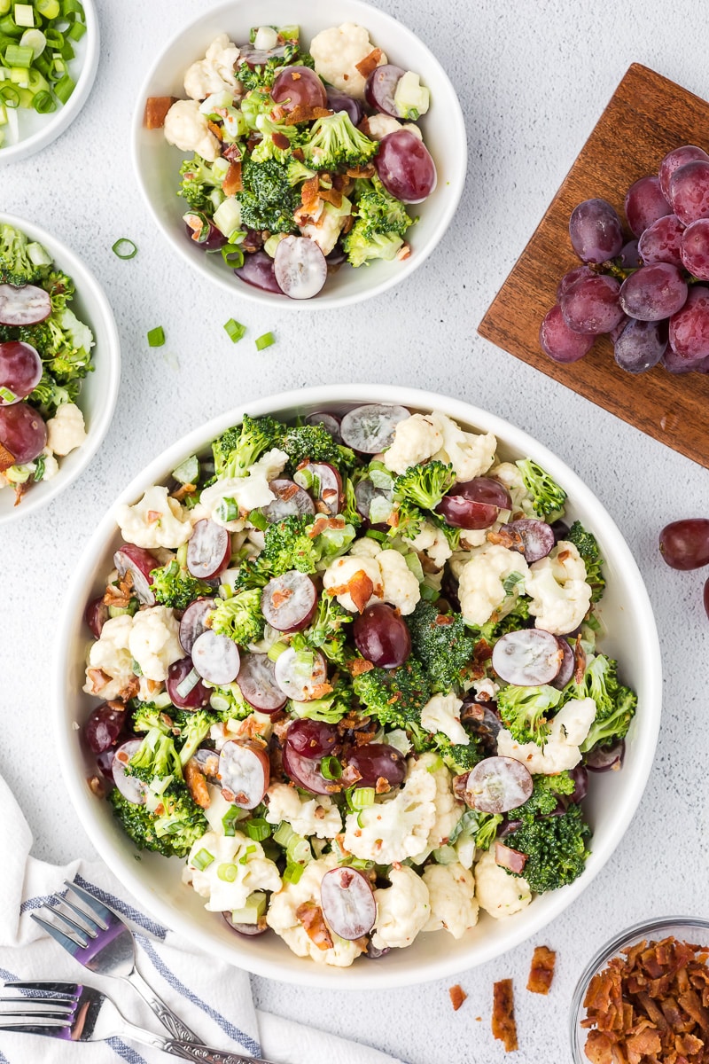 Broccoli Salad with bacon in a white bowl with two small serving bowls full of salad.
