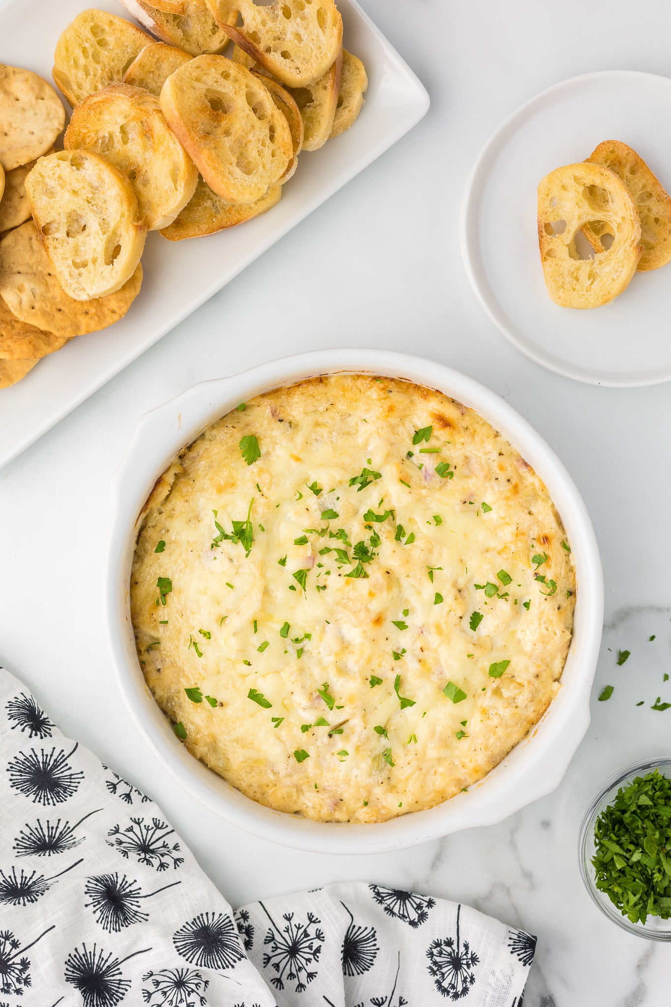 Hot Artichoke Dip in a baking dish sprinkled with fresh parsley.