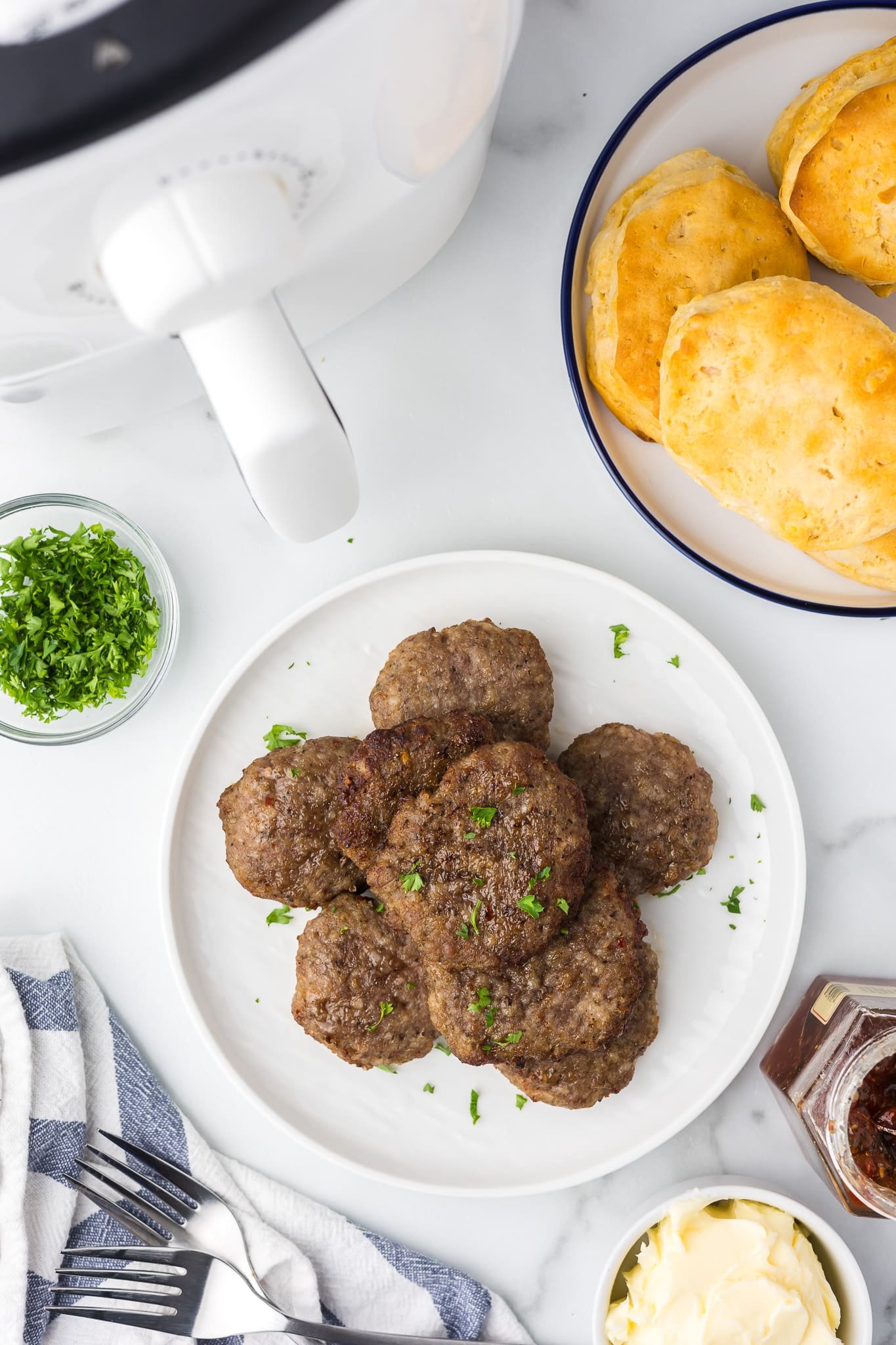 Cooked breakfast sausage on a plate with biscuits, butter and jelly.