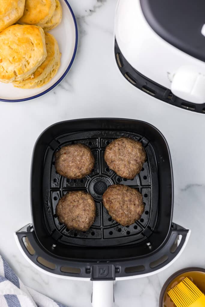 Cooked air fryer sausage patties in an air fryer basket with biscuits and an air fryer.