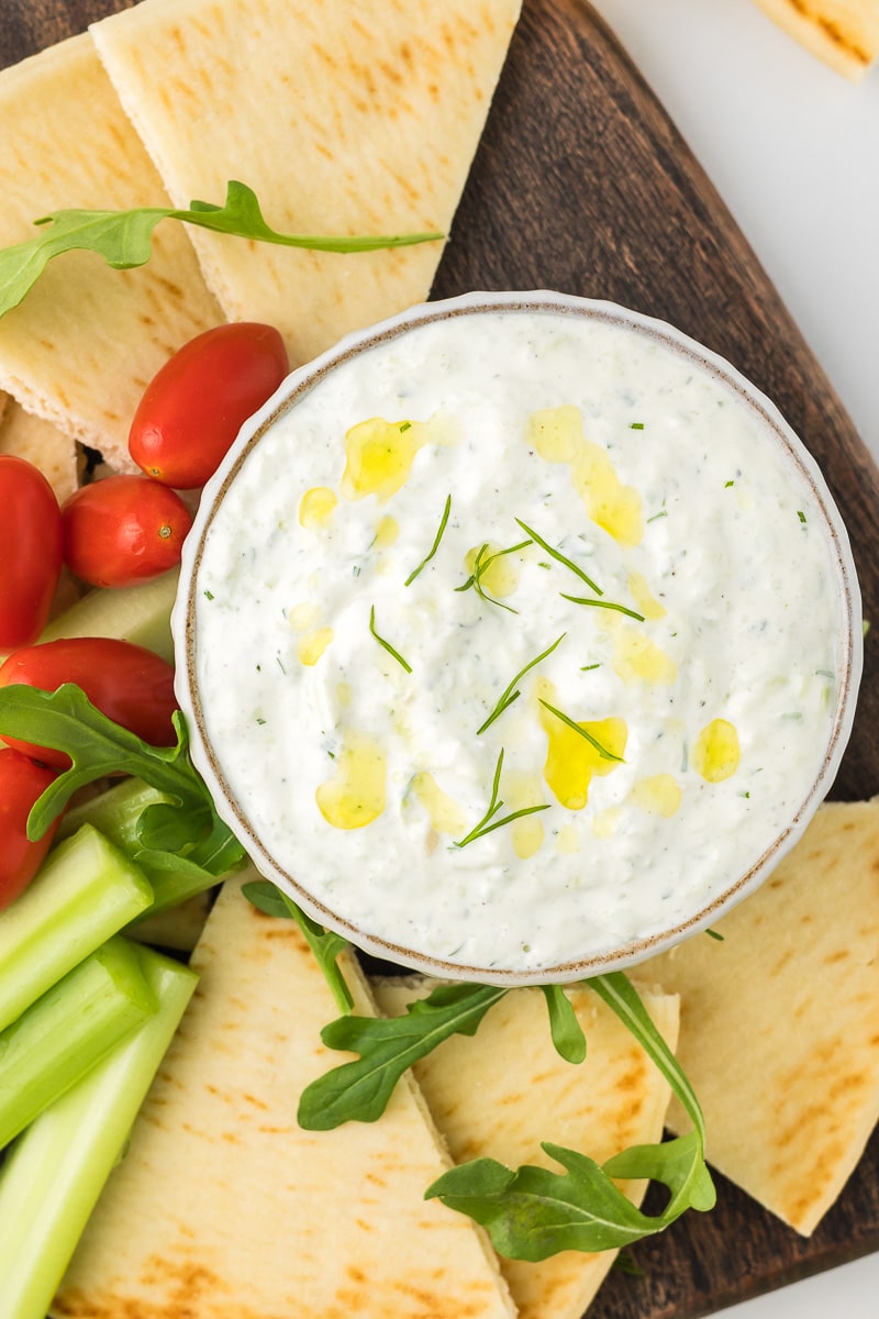 Tzatziki sauce on a cutting board with celery, tomatoes, and pita bread.