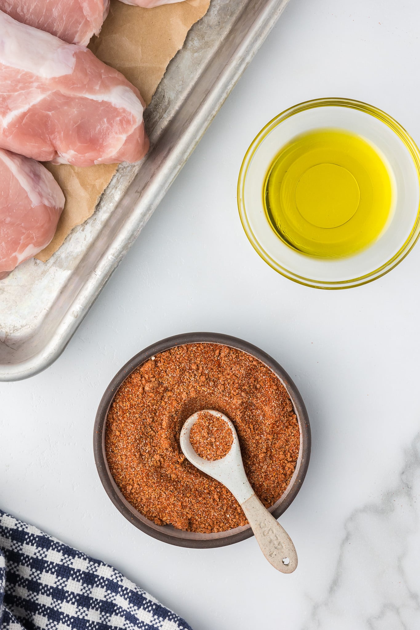 Spice blend for air fryer pork chops in a bowl with olive oil and pork chops.