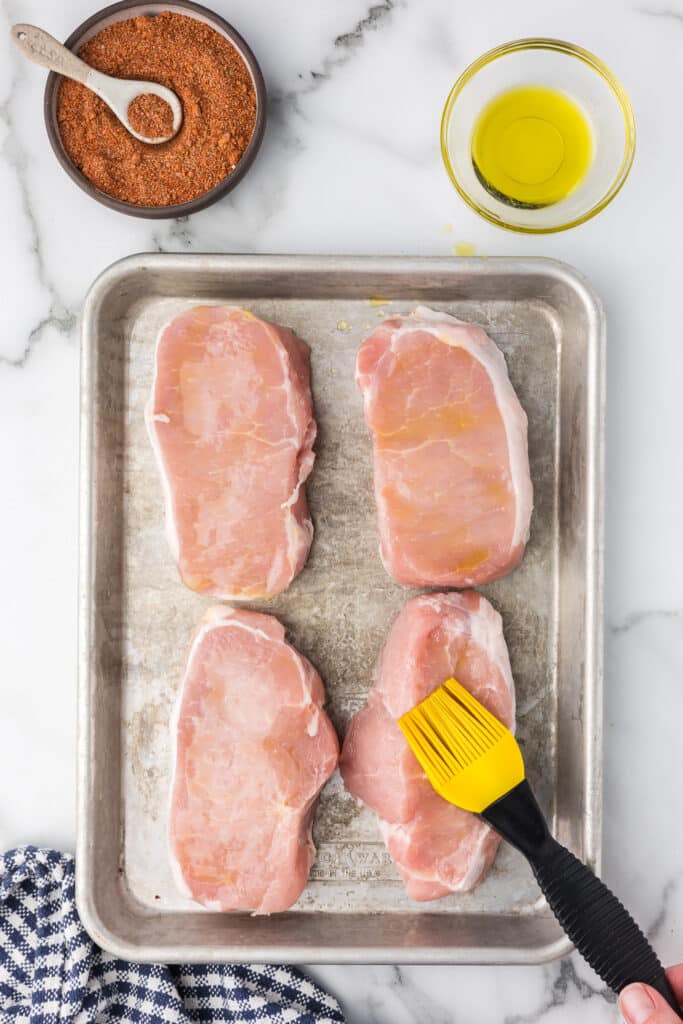 Pork chops with a olive oil being added with a brush.