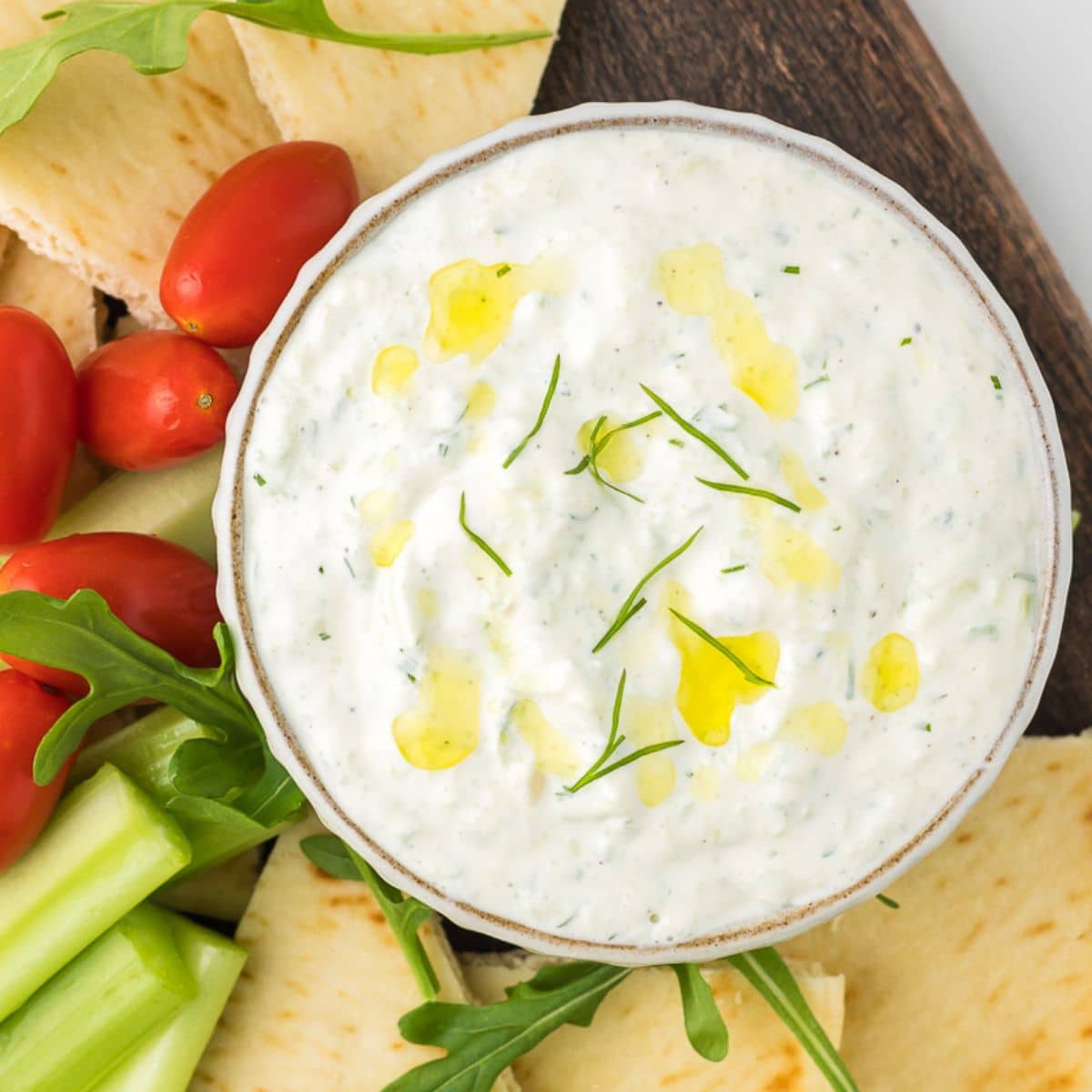 Tzatziki sauce in a bowl with pita bread and vegetables.