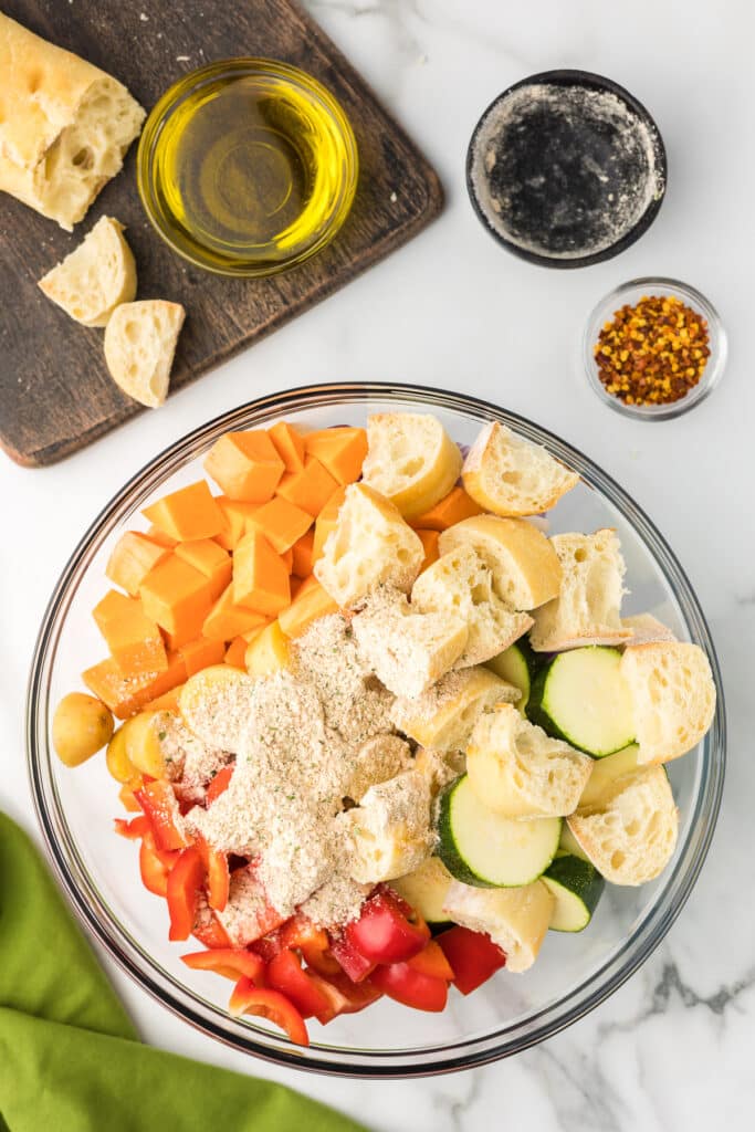 Vegetables and bread in a bowl with spice mix for sheet pan sausage and veggie recipe.