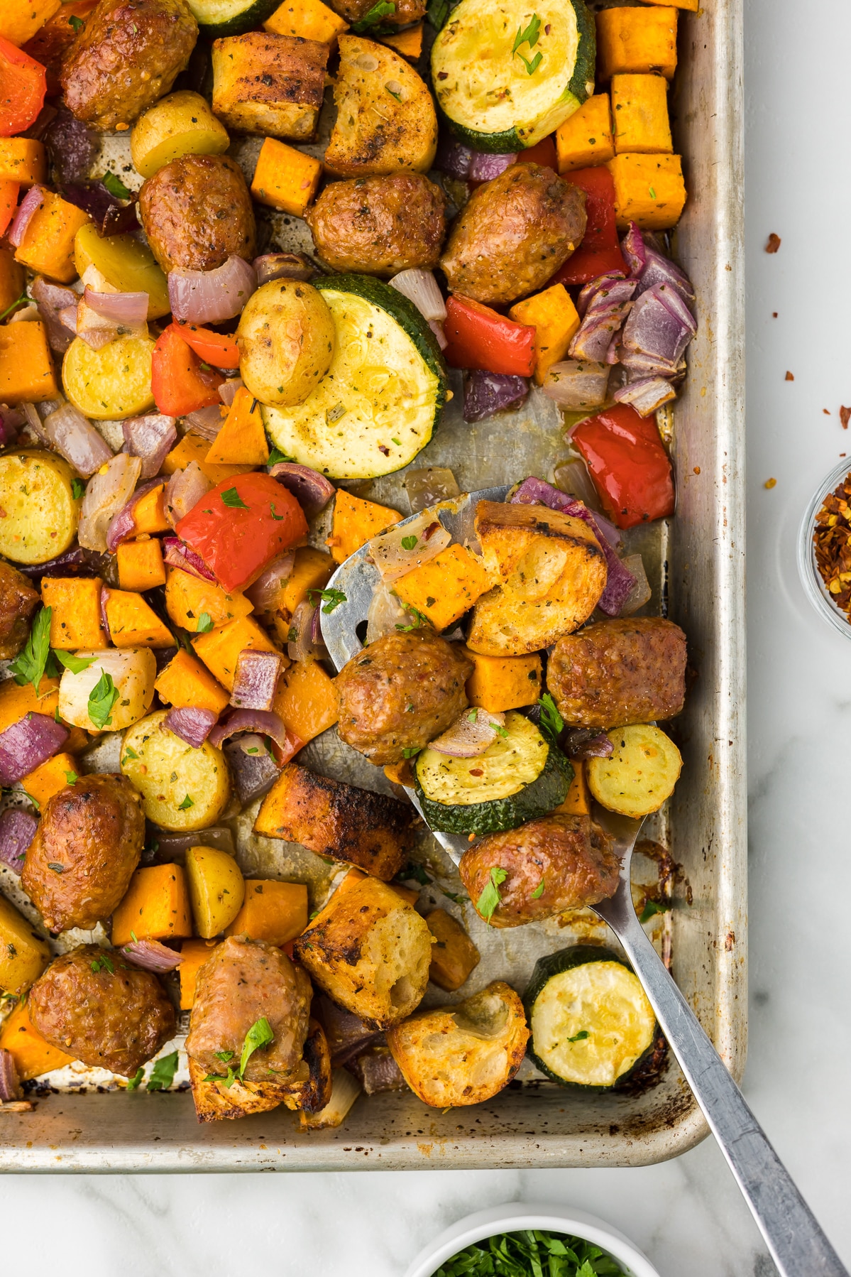 Sheet Pan Sausage and Veggies with a spatula after coming out of the oven.