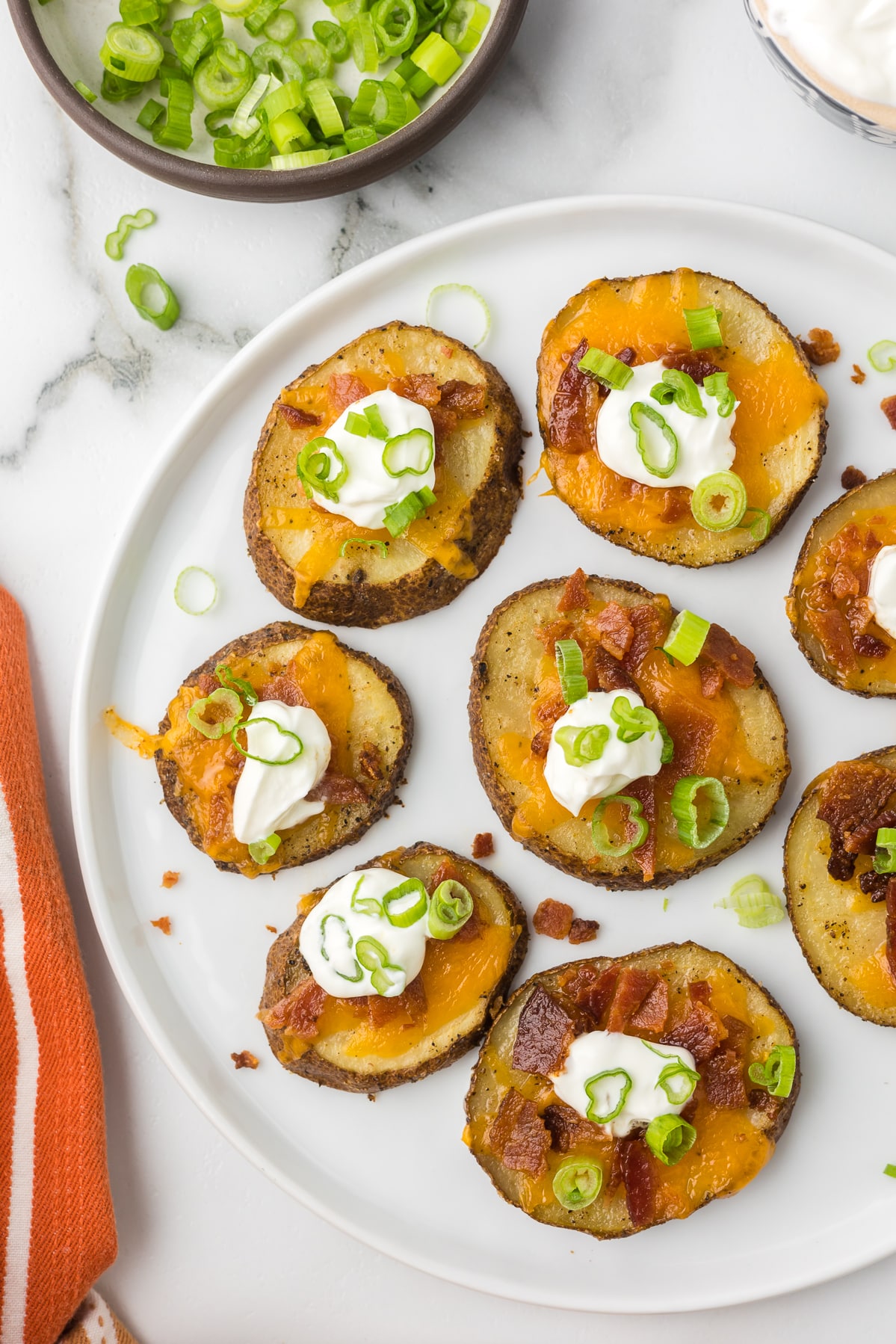Potato bites on a white plate with sour cream, bacon, cheese and green onions.