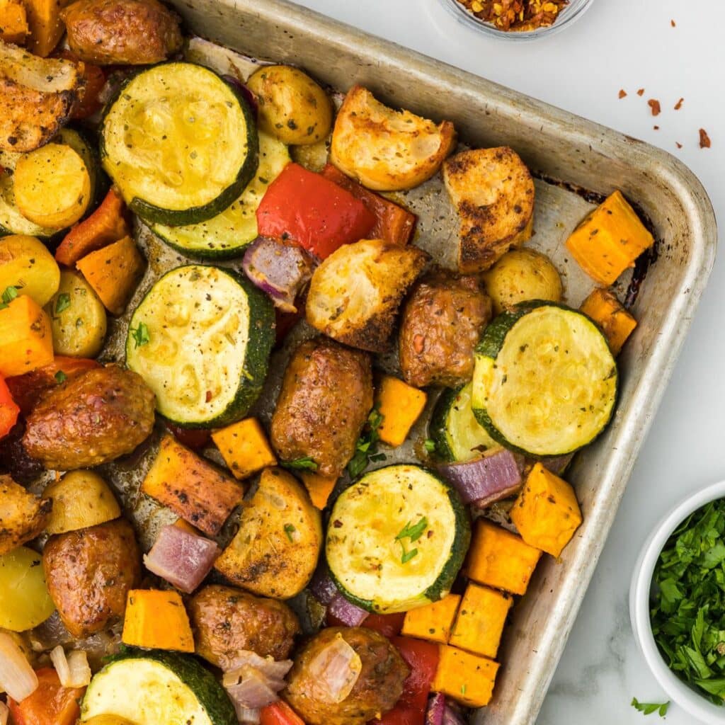 Sausage and veggies on a sheet pan with parsley and red pepper flakes.