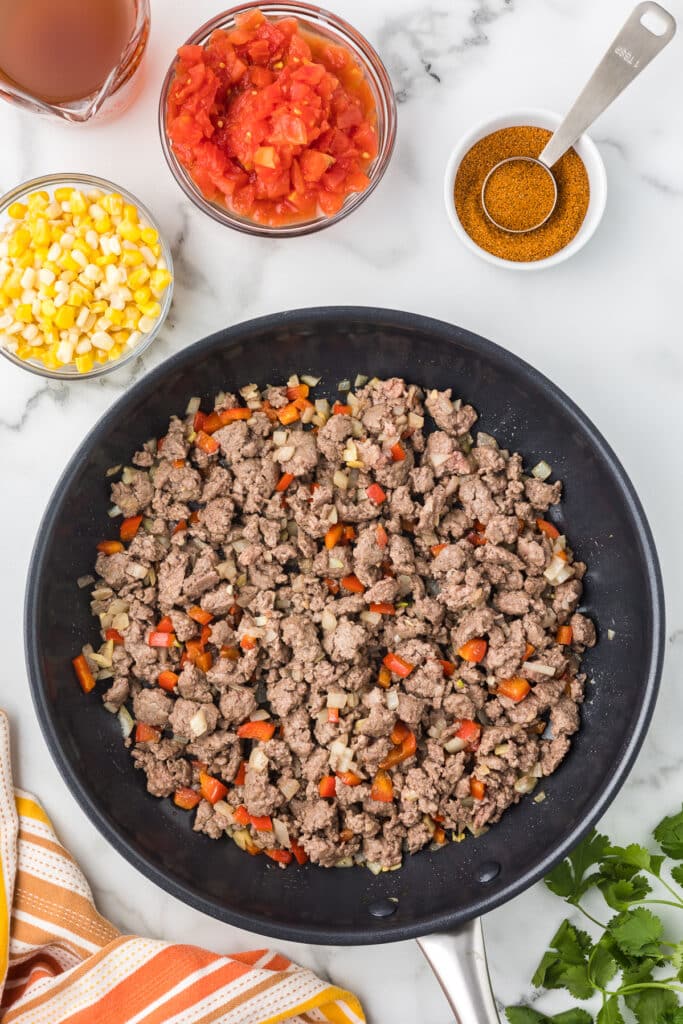 Cooked ground beef, onions and red bell pepper in a skillet.