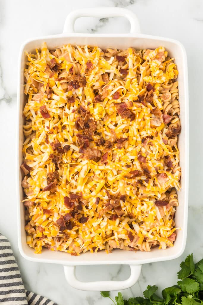Leftover BBQ Chicken Pasta in a casserole dish with cheese and bacon added before baking.