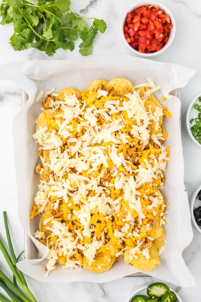 Tortilla chips on a sheet pan with ground chicken and cheese.