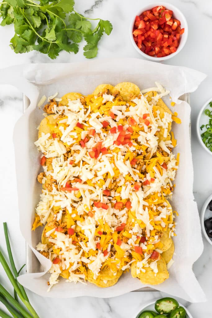 Tortilla chips on a sheet pan with ground chicken, cheese and red bell peppers.