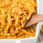 Baked Chicken Parmesan with Penne Pasta in a white casserole dish with a serving spoon.