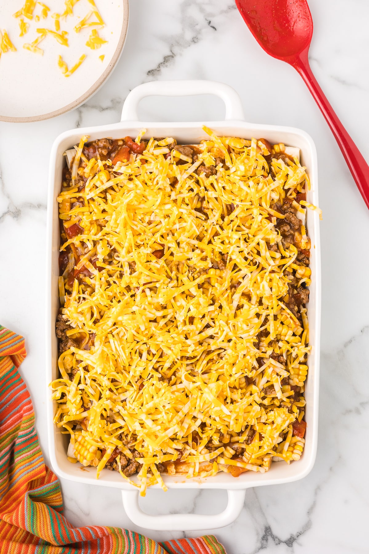 Cream cheese enchilada casserole with cheese before baking.