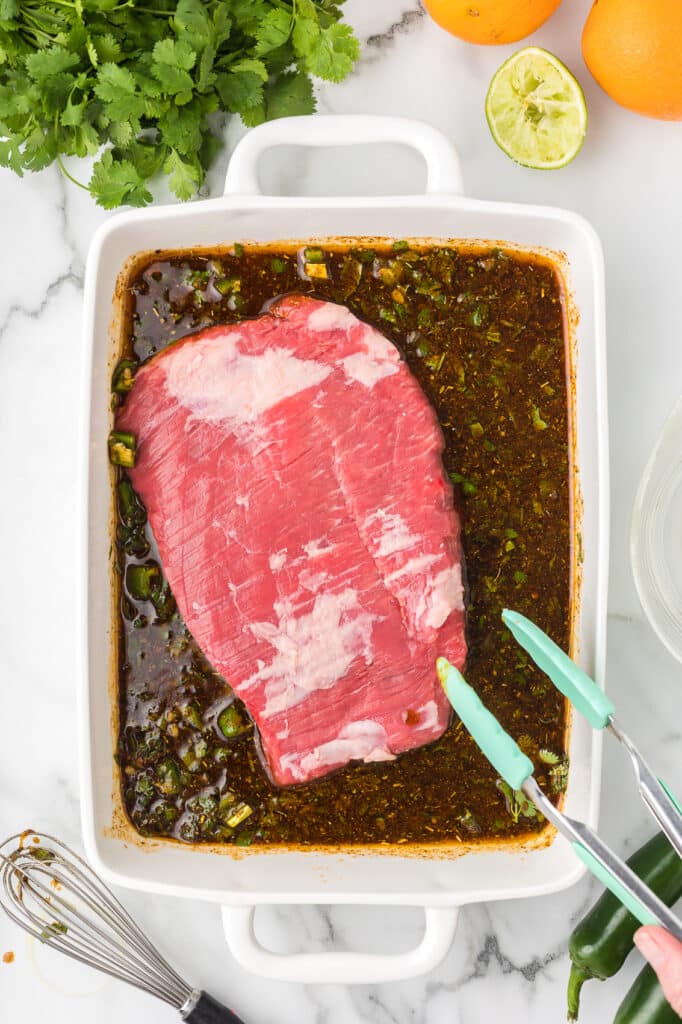 Flank steak and marinade in a white baking dish.