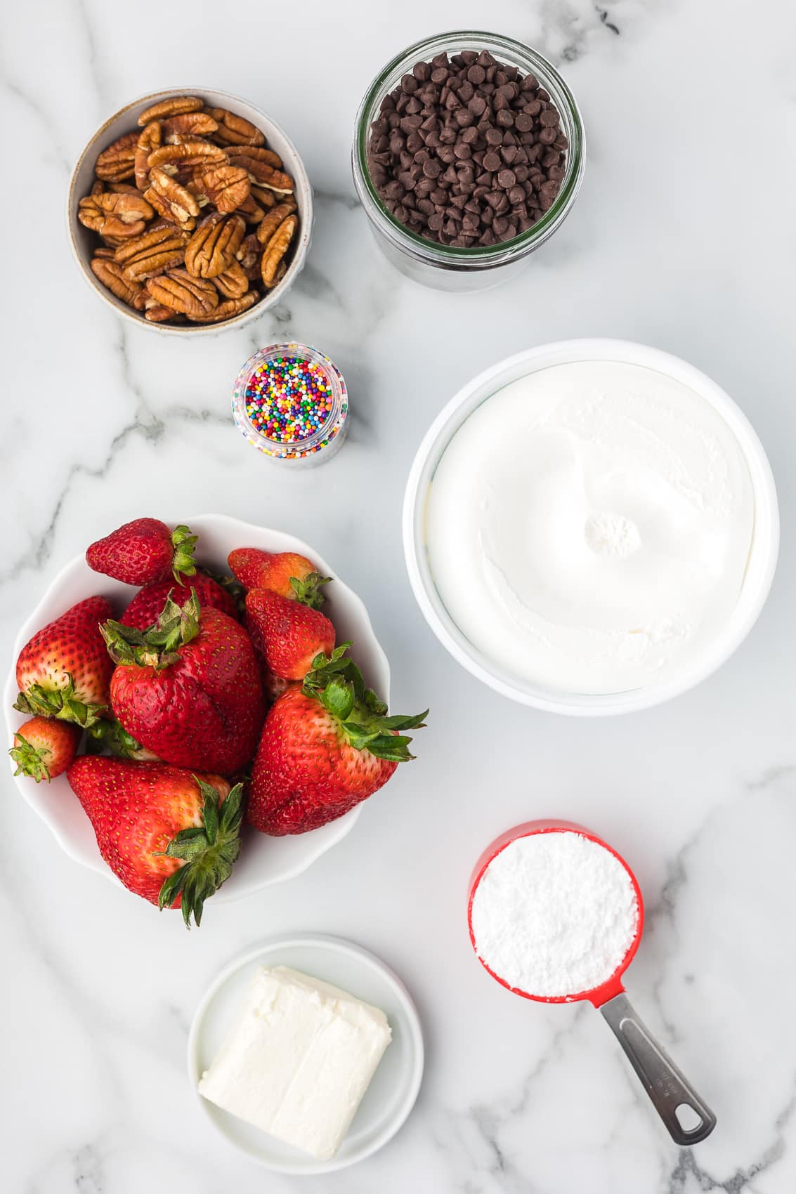 Ingredients to make deviled strawberries including strawberries, toppings, cream cheese, prepared whip topping and powdered sugar.