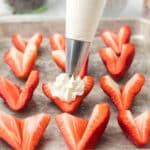 Piping bag with a star tip adding cream cheese mixture to a strawberry.