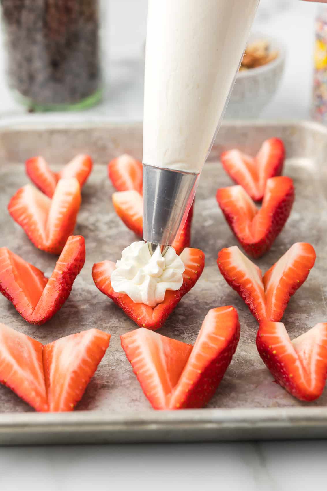 Piping bag with a star tip adding cream cheese mixture to a strawberry.
