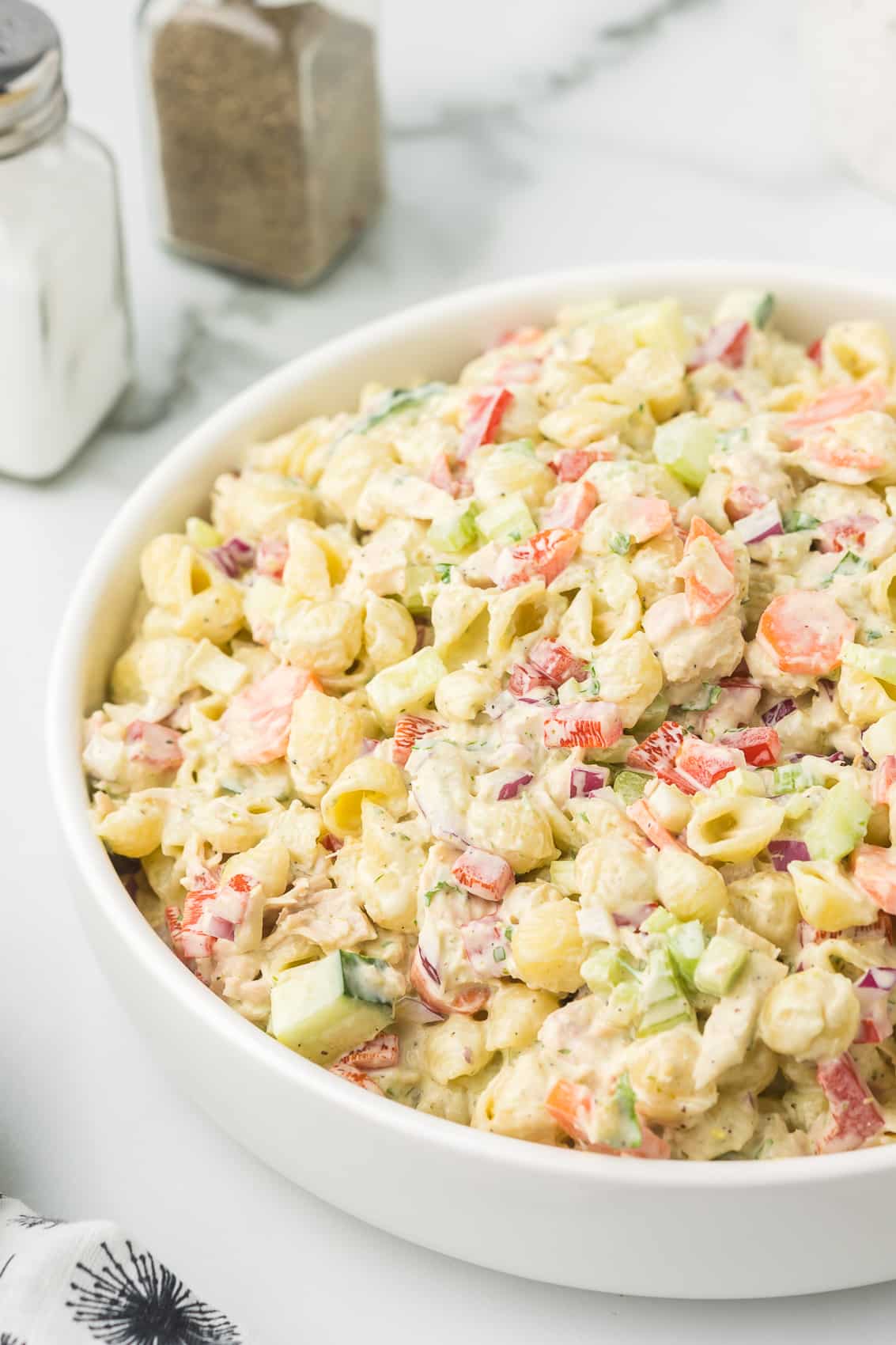 Pesto Pasta Tuna Salad in a white bowl with salt and pepper shakers.