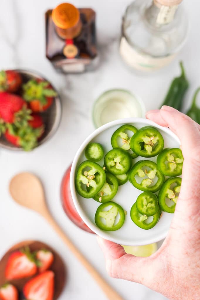 Jalapenos being added to a cocktail shaker.