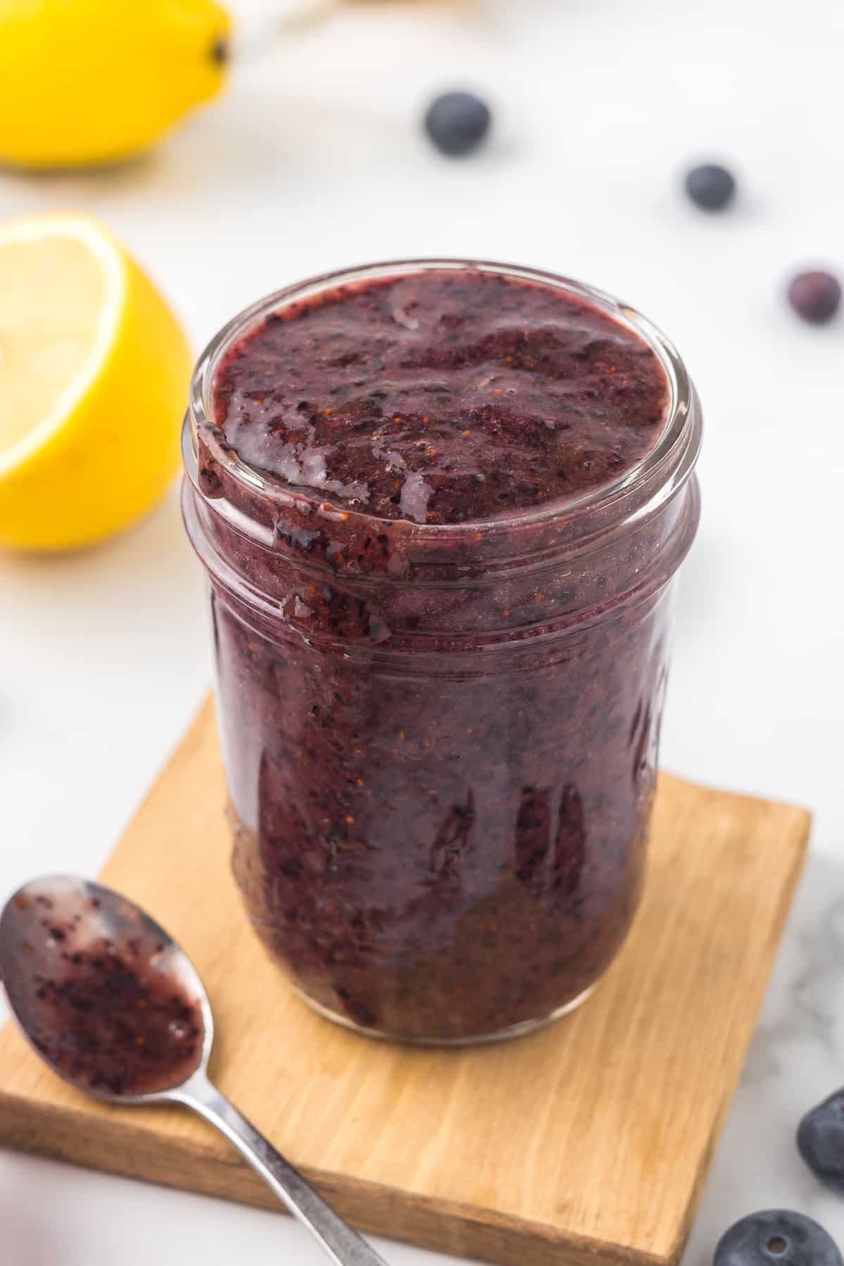 Blueberry Puree in a mason jar with a small spoon on a cutting board.