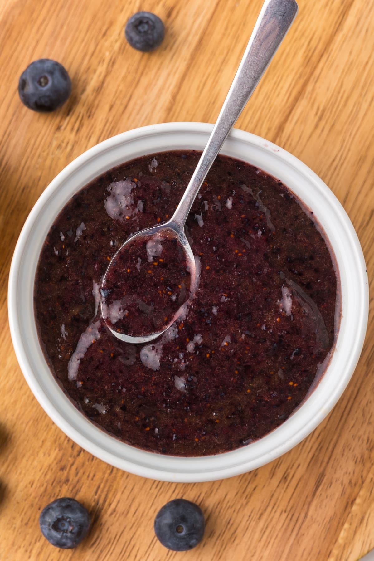 Blueberry puree in a white bowl with a spoon on a cutting board.